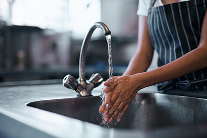 A hospitality staff filling a glass of water from a kitchen tap.